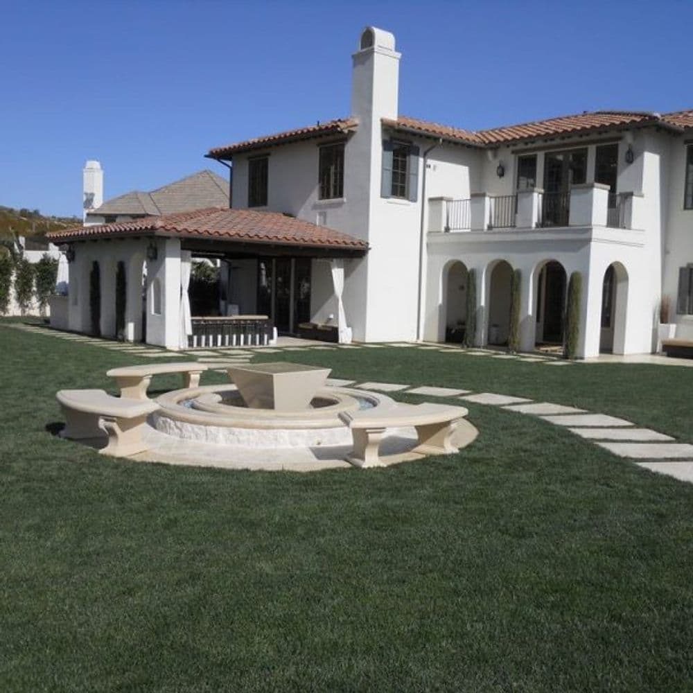Elegant suburban home with patio, fire pit, and landscaped lawn under a clear blue sky.