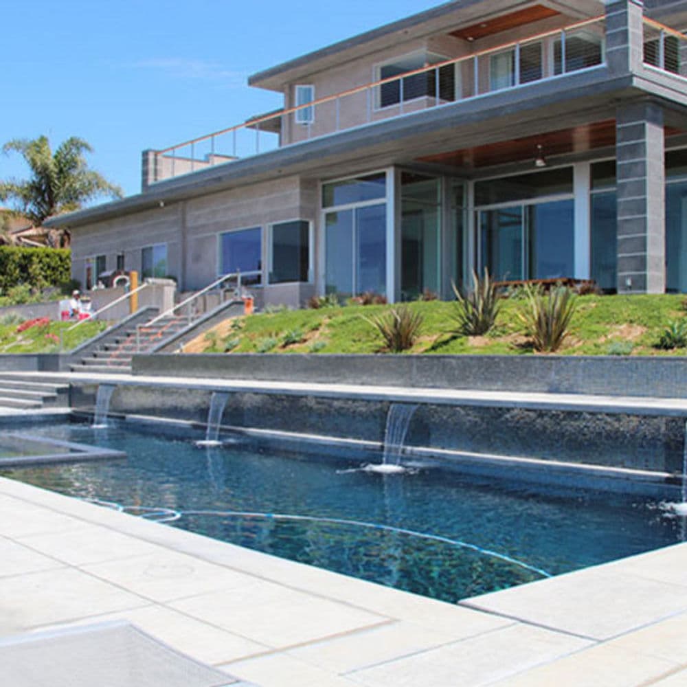 Modern luxury home with a pool and waterfall features surrounded by landscaping.