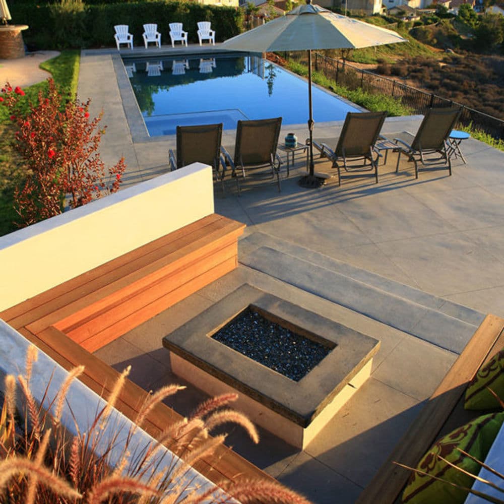 Modern outdoor patio with pool, lounge chairs, and fire pit overlooking scenic landscape.