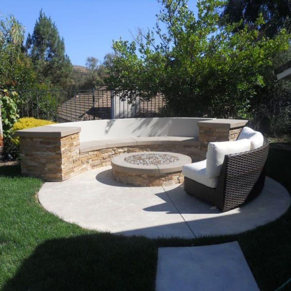 Curved stone seating area with fire pit in a lush backyard setting.