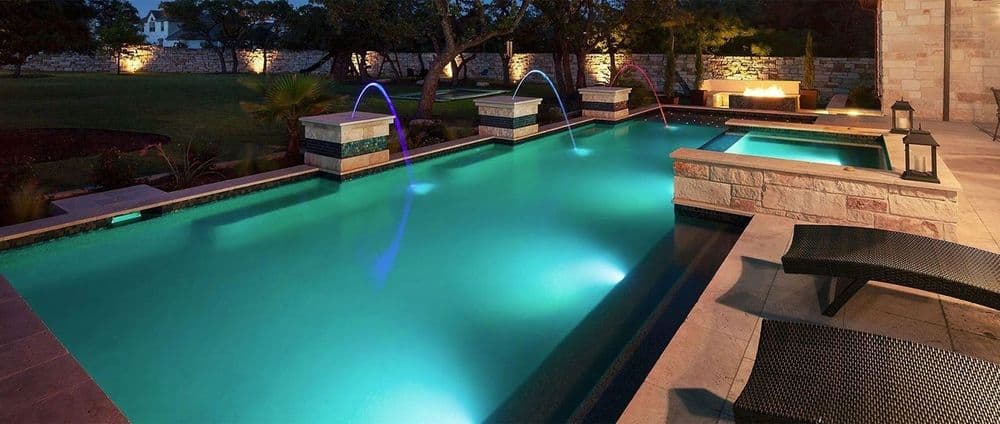 Luxury backyard pool at night with colorful water features and ambient lighting.