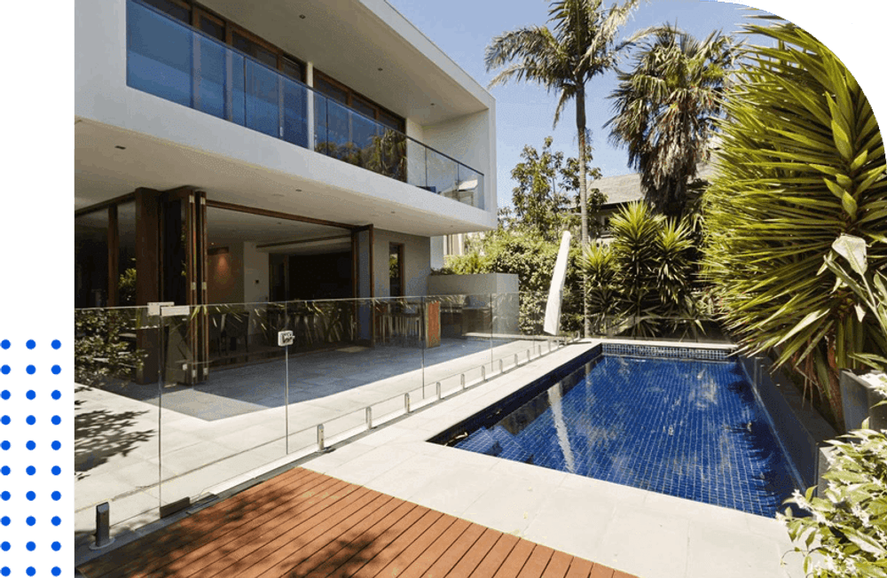Modern home exterior with swimming pool and tropical landscaping in bright sunlight.
