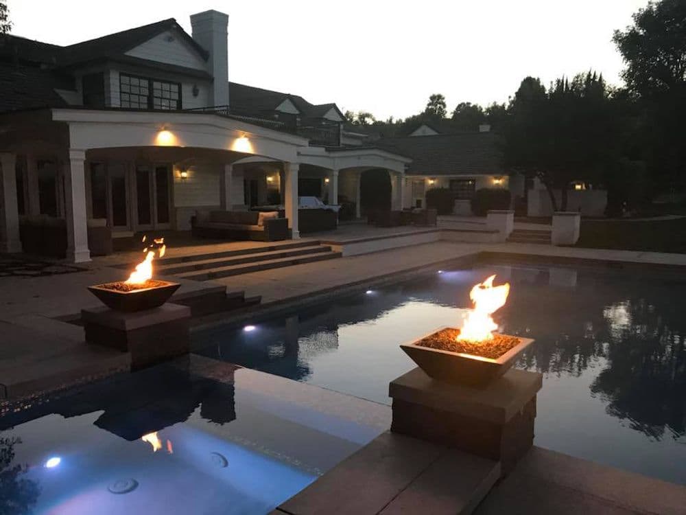 Luxurious home with pool, fire pits, and elegant outdoor living space at dusk.
