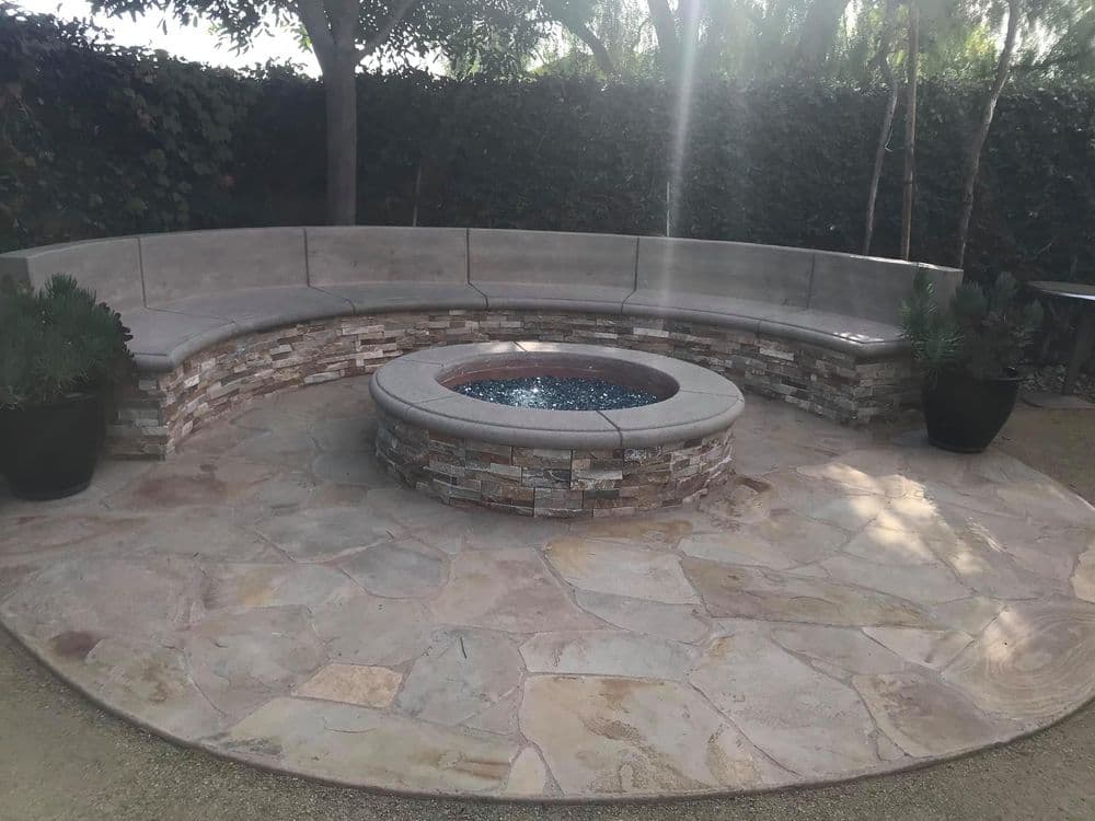 Outdoor patio featuring stone fire pit and curved seating area surrounded by lush greenery.